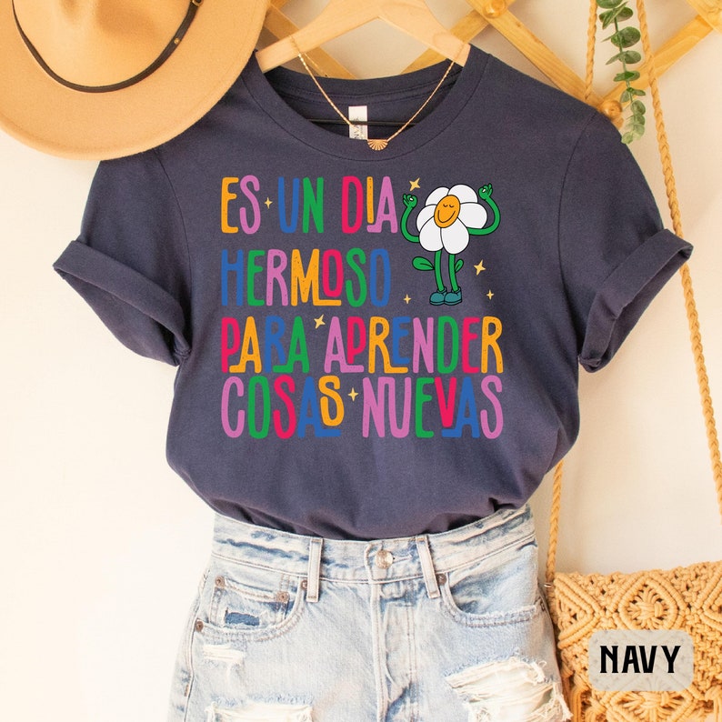 May include: Navy blue t-shirt with a colorful graphic of a flower with the text "Es un dia hermoso para aprender cosas nuevas".