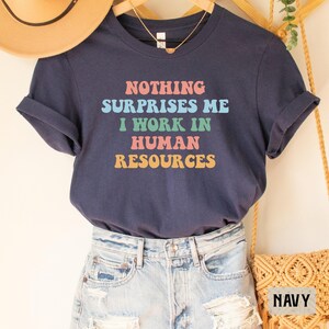 May include: Navy blue t-shirt with the text "NOTHING SURPRISES ME I WORK IN HUMAN RESOURCES" in colorful retro font.