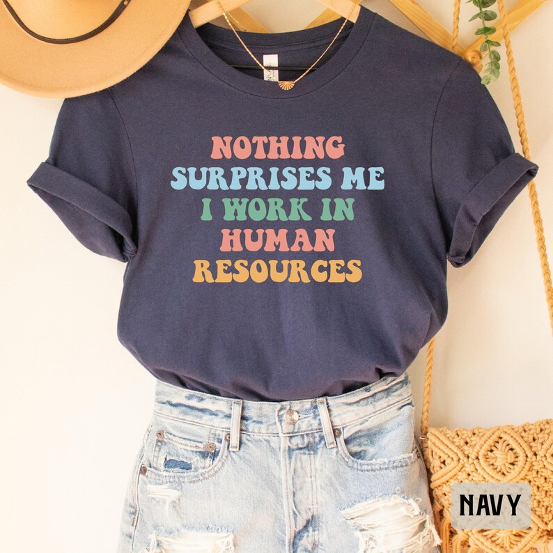 May include: Navy blue t-shirt with the text "NOTHING SURPRISES ME I WORK IN HUMAN RESOURCES" in colorful retro font.