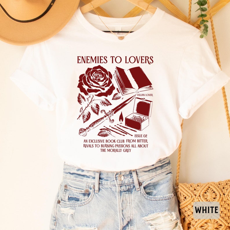 May include: White t-shirt with a red graphic design featuring a rose, a book, a dagger, matches, and the text "Enemies to Lovers" and "Villain Lover". The text below the graphic reads "Issue 02 An Exclusive Book Club From Bitter Rivals to Burning Passions All About The Morally Grey".