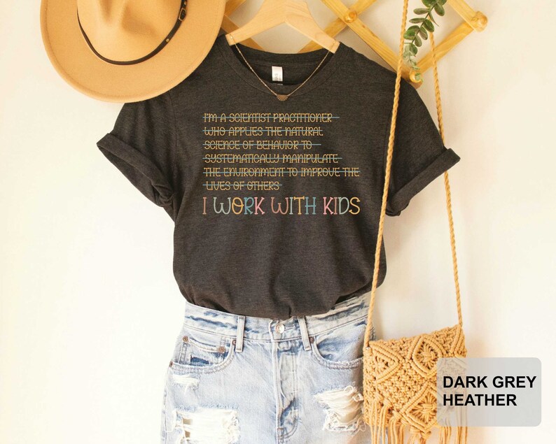May include: Dark grey heather t-shirt with the text "I'm a scientist practitioner who applies the natural science of behavior to systematically manipulate the environment to improve the lives of others I work with kids".