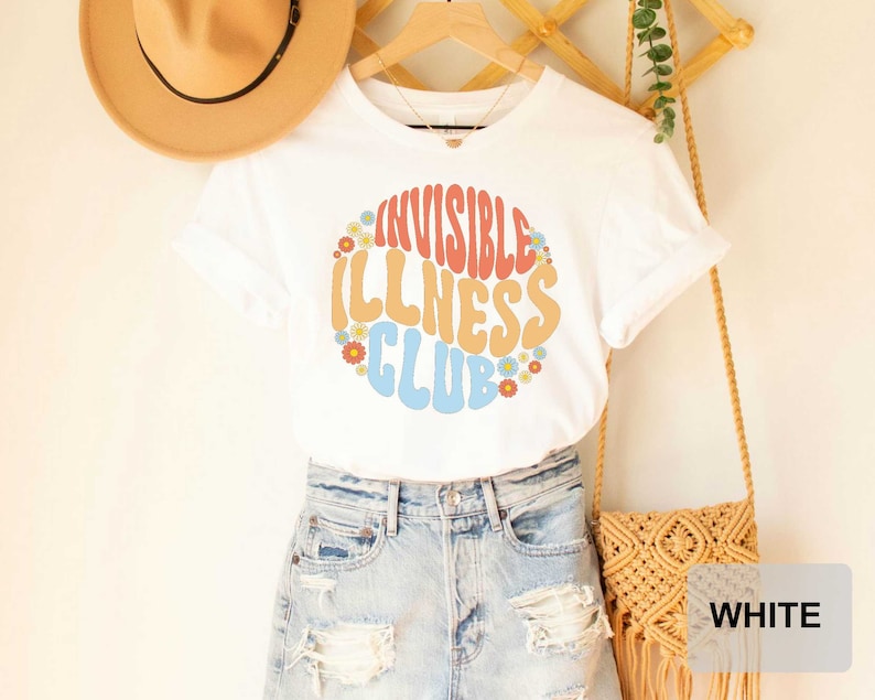 K&ouml;nnte beinhalten: Wei&szlig;es T-Shirt mit einer bunten Grafik, auf der "Invisible Illness Club" mit Blumen um den Text steht.