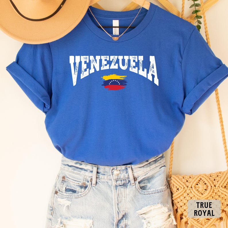 May include: A royal blue t-shirt with the word "VENEZUELA" in white distressed lettering and a small Venezuelan flag graphic. The shirt is made of a soft, comfortable material.