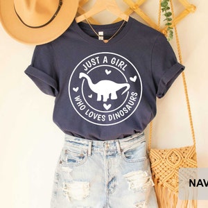 Puede incluir: Camiseta azul marino con un gr&aacute;fico blanco de un dinosaurio y el texto "Just a girl who loves dinosaurs".