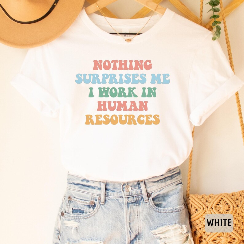 May include: White t-shirt with the text "NOTHING SURPRISES ME I WORK IN HUMAN RESOURCES" in rainbow colors.