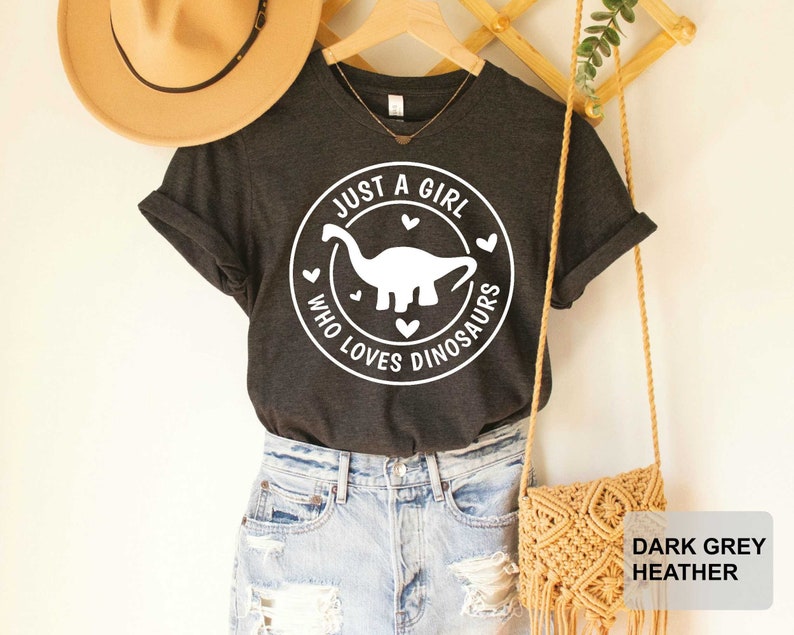 Puede incluir: Camiseta de color gris oscuro jaspeado con un gr&aacute;fico blanco de un dinosaurio y el texto "Just a girl who loves dinosaurs".