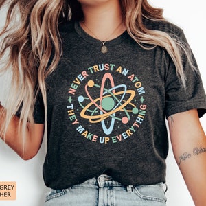May include: Dark grey heather t-shirt with a graphic of an atom and the text "Never trust an atom they make up everything".