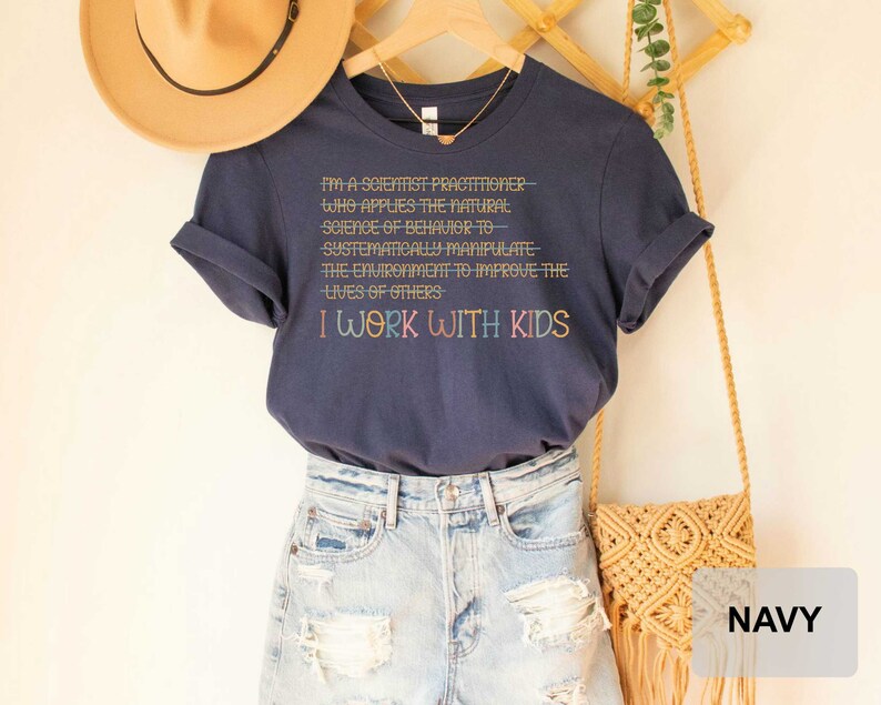 May include: Navy blue t-shirt with the text "I'm a scientist practitioner- who applies the natural science of behavior to systematically manipulate the environment to improve the lives of others I work with kids".