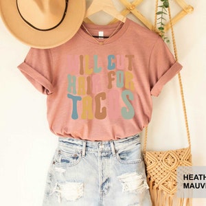 May include: A heather mauve t-shirt with the text "I'll cut hair for tacos" in colorful retro font.