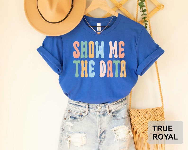 May include: A royal blue t-shirt with the text "Show Me The Data" in rainbow colors. The shirt is being modeled with a straw hat and denim shorts.