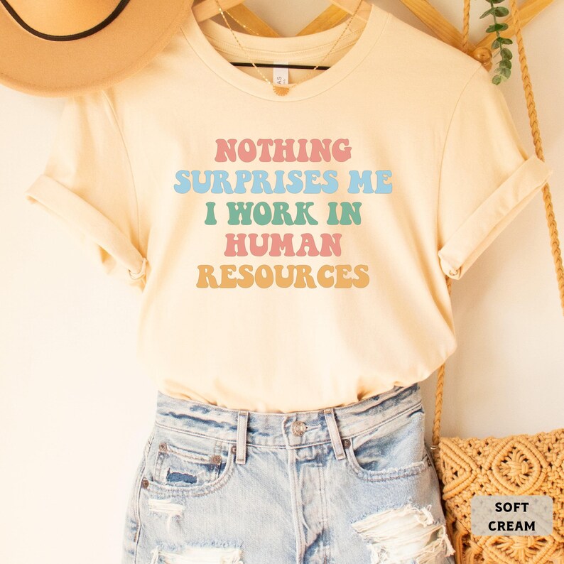 May include: A soft cream colored t-shirt with the text "Nothing Surprises Me I Work In Human Resources" in rainbow colors.
