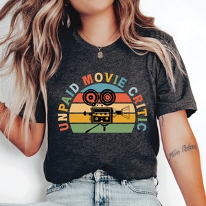 May include: A dark gray t-shirt with a vintage-style graphic of a film camera and the text "Unpaid Movie Critic" in a circle.