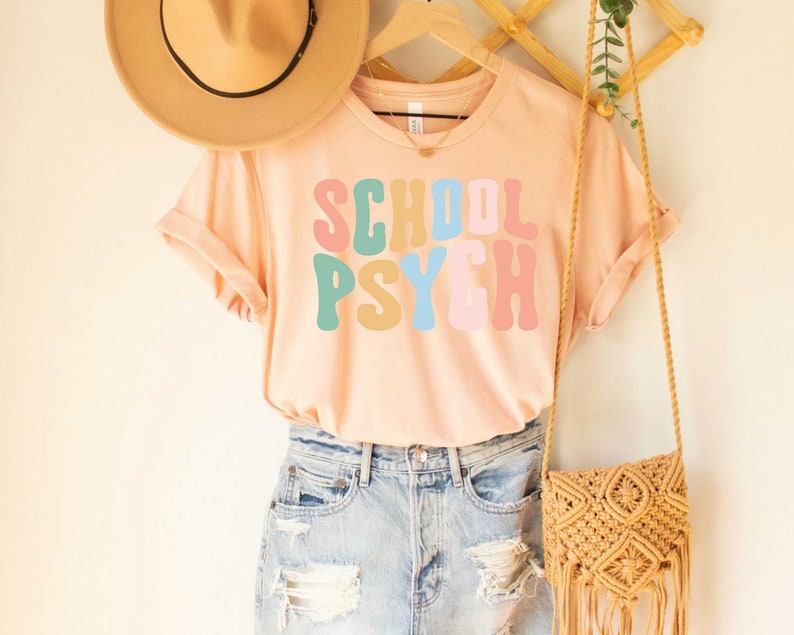 May include: A light pink t-shirt with the words "SCHOOL PSYCH" in colorful, retro-style lettering.