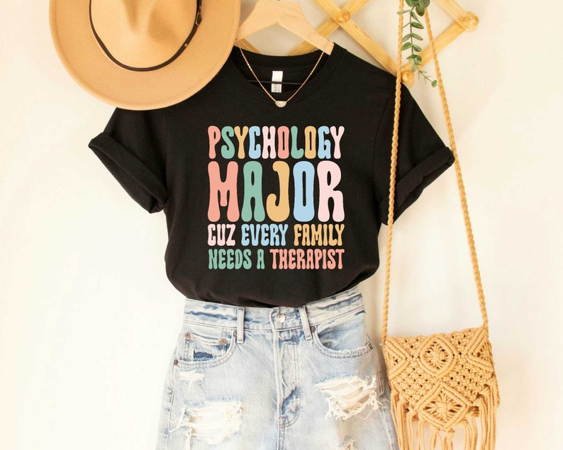 May include: Black t-shirt with the text "Psychology Major Cuz Every Family Needs A Therapist" in colorful retro font.