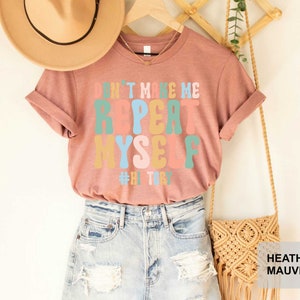 May include: A heather mauve t-shirt with the text "Don't make me repeat myself #hitry" in colorful, retro-style lettering.