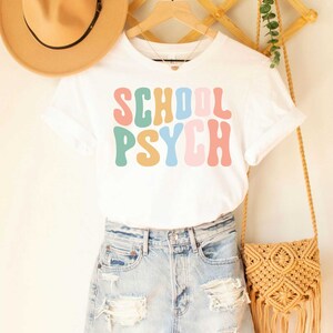 May include: White t-shirt with the text "SCHOOL PSYCH" in colorful retro font.