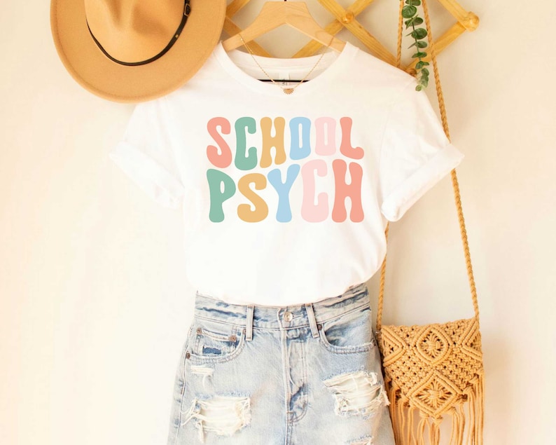 May include: White t-shirt with the text "SCHOOL PSYCH" in colorful retro font.