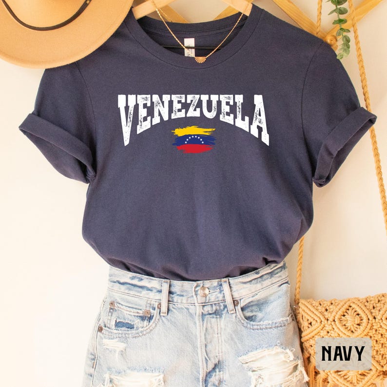 May include: A navy blue t-shirt with the word "VENEZUELA" in white text and a yellow, blue, and red Venezuelan flag graphic.