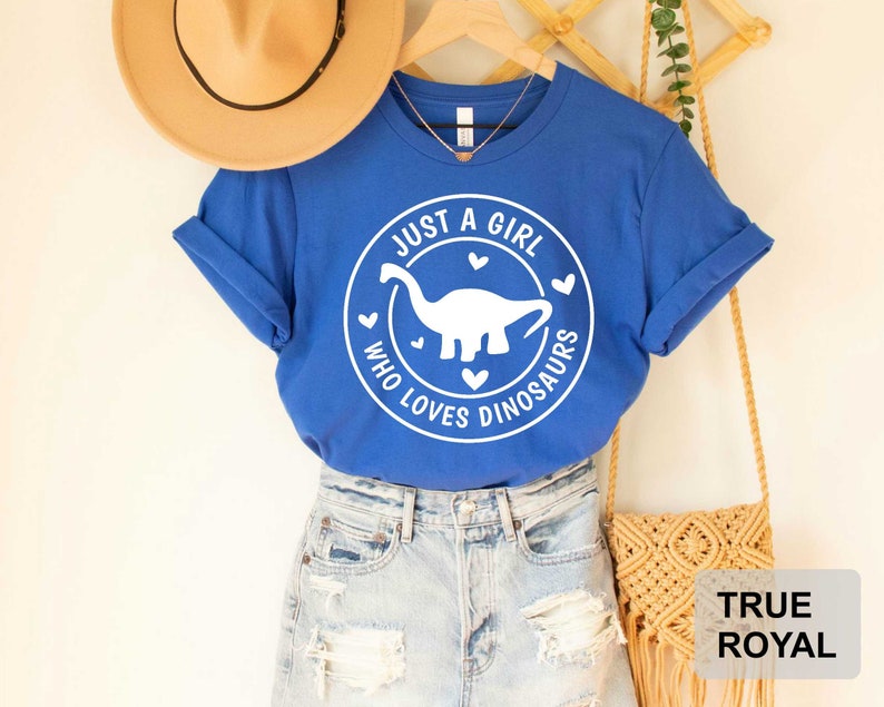 Puede incluir: Una camiseta azul real con un gr&aacute;fico blanco de un dinosaurio y el texto "Just a girl who loves dinosaurs".