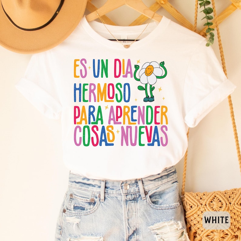 May include: White t-shirt with a colorful graphic of a flower with the text "ES UN DIA HERMOSO PARA APRENDER COSAS NUEVAS".
