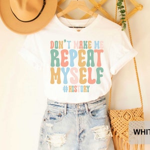 May include: White t-shirt with a colorful graphic that says "Don't Make Me Repeat Myself #History".