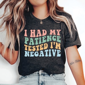 Może przedstawiać: Szary t-shirt z napisem "I had my patience tested I'm negative" w kolorach tęczy. Tekst jest w retro stylu czcionki.