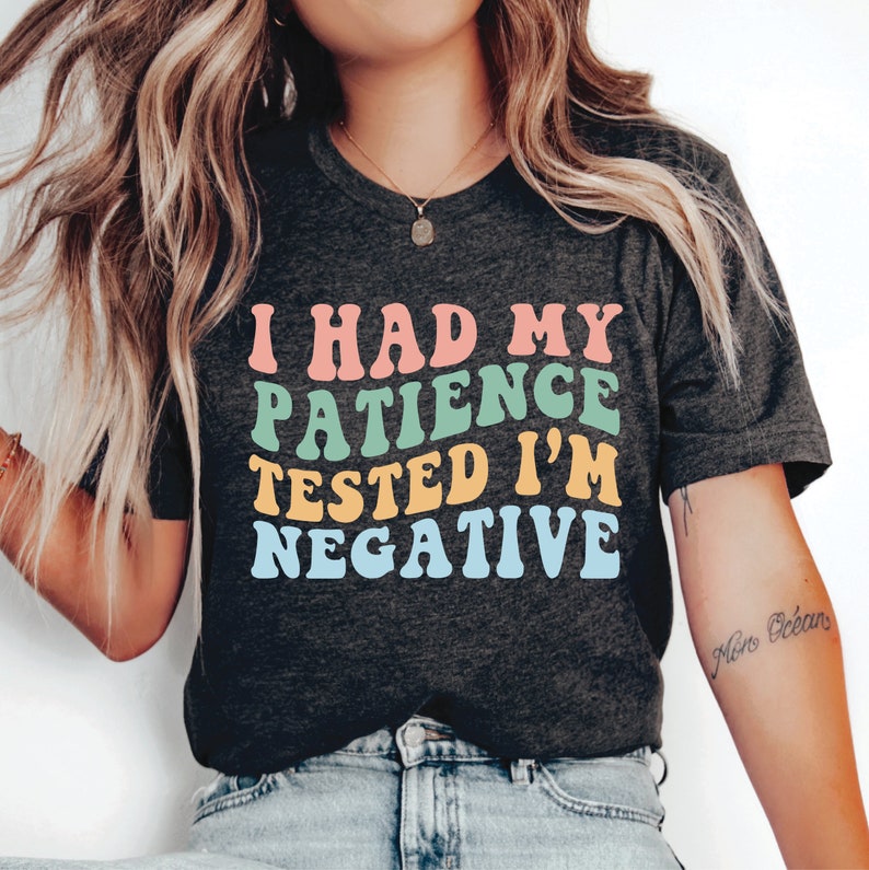 Może przedstawiać: Szary t-shirt z napisem "I had my patience tested I'm negative" w kolorach tęczy. Tekst jest w retro stylu czcionki.