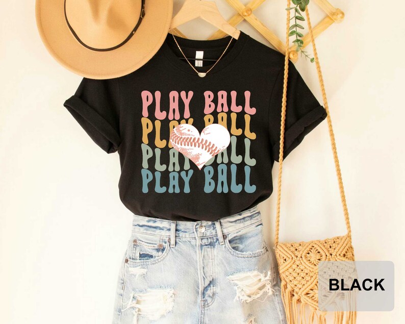 Peut inclure: T-shirt noir avec un graphique r&eacute;tro d'un ballon de baseball en forme de c&oelig;ur et le texte "PLAY BALL" r&eacute;p&eacute;t&eacute; dans diff&eacute;rentes couleurs.