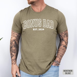 May include: A heather olive t-shirt with the text "BONUS DAD EST. 2024" in white.