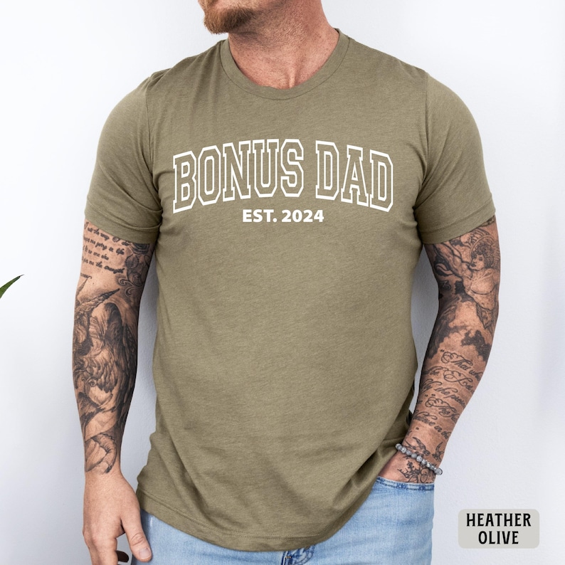 May include: A heather olive t-shirt with the text "BONUS DAD EST. 2024" in white.