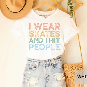 May include: White t-shirt with the text "I wear skates and I hit people" in rainbow colours. The shirt is being modelled by a person wearing denim shorts.
