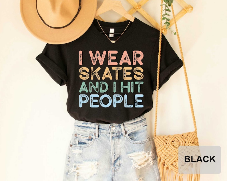 May include: Black t-shirt with the text "I wear skates and I hit people" in rainbow colours. The shirt is being modelled with a straw hat and a brown woven bag.