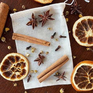 Peut inclure: Une composition d'épices aromatiques et d'agrumes séchés sur une surface en bois foncé. L'arrangement comprend de l'anis étoilé, des bâtons de cannelle, des clous de girofle, des tranches d'orange séchées et un petit sac en lin.