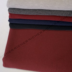 May include: Stack of six different coloured knit fabrics. The fabrics are in the following order from top to bottom: light grey, dark grey, burgundy, navy blue, black, and burgundy.