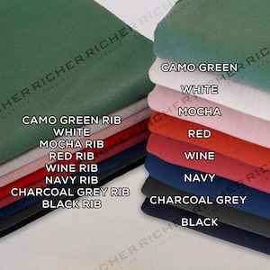 Op de afbeelding: Een stapel stofstalen in verschillende kleuren en texturen, waaronder camouflagegroen, wit, mokka, rood, wijn, marine, antracietgrijs en zwart. Elk staal heeft een label met de kleur en het type, zoals "Camo Green Rib" en "Black Rib".