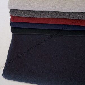 May include: A stack of different coloured fabric swatches. The swatches are folded and layered on top of each other. The top swatch is a light grey, followed by a dark grey, a burgundy, a navy blue, a black, and a dark blue.