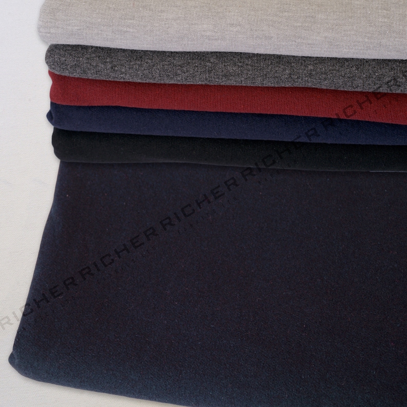 May include: A stack of different coloured fabric swatches. The swatches are folded and layered on top of each other. The top swatch is a light grey, followed by a dark grey, a burgundy, a navy blue, a black, and a dark blue.