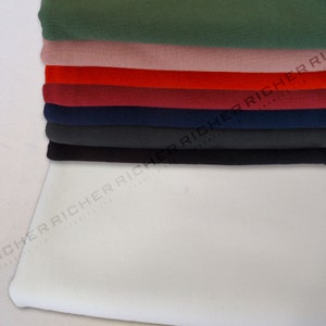Op de afbeelding: Een stapel stofstalen in verschillende kleuren, waaronder groen, roze, rood, bordeauxrood, donkerblauw, zwart en wit. De stof is glad en lijkt een lichtgewicht materiaal te zijn.