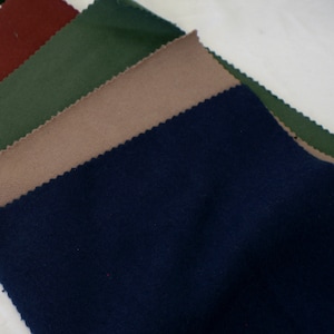 Op de afbeelding: Vier stofstalen in verschillende kleuren: donkerrood, bosgroen, lichtbruin en marineblauw. De stalen zijn in een stapel gerangschikt, met de donkerrode staal bovenop en de marineblauwe staal onderaan.