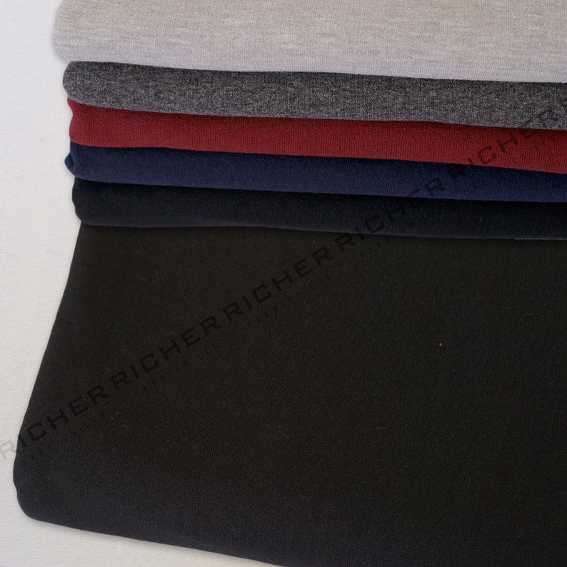 May include: A stack of different coloured fabric swatches. The swatches are folded and arranged in a pile. The top swatch is a light grey, followed by a dark grey, a burgundy, a navy blue, and a black swatch.