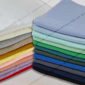 May include: A stack of fabric swatches in various colours, including white, light blue, green, and navy blue. The fabric is smooth and appears to be cotton. The swatches are stacked on a white surface. The text "RICHER-FABRICS.CO.UK" is visible on the fabric.