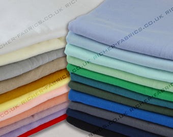 Op de afbeelding: Een stapel stofstalen in verschillende kleuren, waaronder wit, lichtblauw, groen en donkerblauw. De stof is glad en lijkt van katoen te zijn. De stalen zijn gestapeld op een wit oppervlak. De tekst "RICHER-FABRICS.CO.UK" is zichtbaar op de stof.