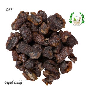 May include: A close-up of a pile of dark brown, irregularly shaped resin pieces. The resin is called "Pipal Lakh" and is labeled "OSI Organic Store India".