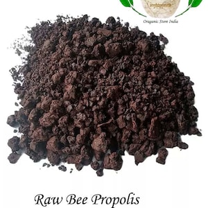 May include: A close-up of a pile of dark brown, irregularly shaped pieces of raw bee propolis. The propolis is a natural resin produced by honeybees. The text "Raw Bee Propolis" is written below the pile of propolis.