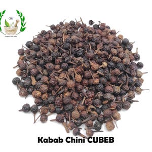 Könnte beinhalten: Nahaufnahme eines Haufens getrockneter schwarzer und brauner Cubeben-Pfefferkörner. Die Pfefferkörner sind klein und rund, mit einer leicht runzeligen Textur. Der Text "Kabab Chini CUBEB" ist unter dem Haufen Pfefferkörner gedruckt.