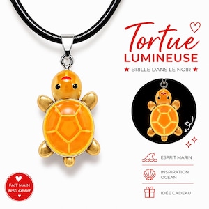 Peut inclure: Un collier pendentif tortue sur un cordon noir. La breloque tortue est orange avec une finition brillante, des yeux noirs et une bouche rouge. Le texte sur l'image indique Tortue Lumineuse, Brille dans le noir, Esprit Marin, Inspiration Océan, Idée Cadeau et Fait main avec amour.
