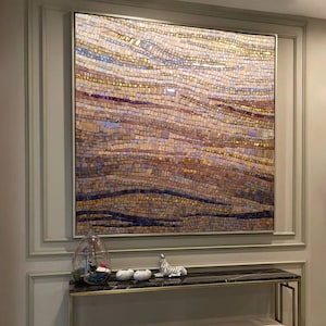 May include: A large mosaic artwork in a gold frame hangs above a black marble console table with gold legs. Two upholstered benches with gold legs are in front of the table. Decorative items on the table include a glass terrarium, white spheres, and a zebra figurine.