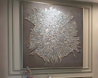 May include: A large, framed abstract artwork with a mosaic design in shades of silver and gold hangs above a black marble console table. Two upholstered stools with gold metal frames are in front of the table. Decorative items are on the table.