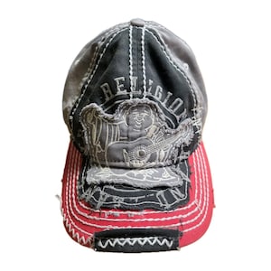May include: A distressed baseball cap with a black and grey crown and a red peak. The cap features white stitching and a patch with the word "RELIGION" and a graphic of a figure playing a guitar.