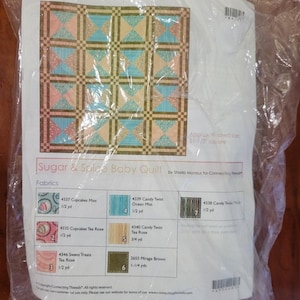 May include: A packaged baby quilt kit titled "Sugar & Spice" with a geometric pattern in shades of pink, blue, and tan. The kit includes fabric swatches and the approximate finished size is 51.5 inches square.